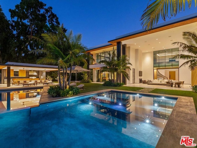 pool at night featuring a patio area and a lawn