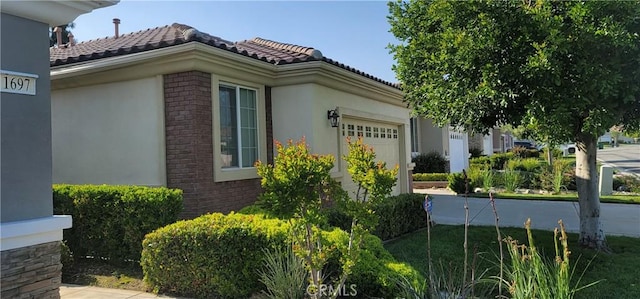 view of side of home with a garage, stucco siding, a tiled roof, and brick siding