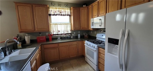 kitchen featuring white appliances, brown cabinetry, dark countertops, a sink, and light tile patterned flooring