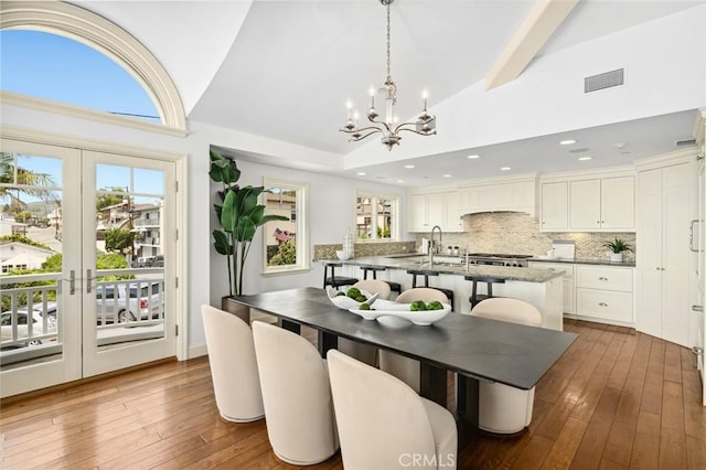 dining space featuring high vaulted ceiling, hardwood / wood-style flooring, visible vents, french doors, and an inviting chandelier