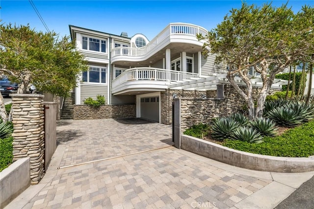 shingle-style home featuring stone siding, decorative driveway, an attached garage, and a balcony