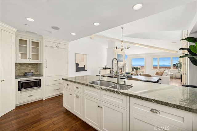 kitchen featuring dark stone countertops, stainless steel microwave, dark wood finished floors, and a sink