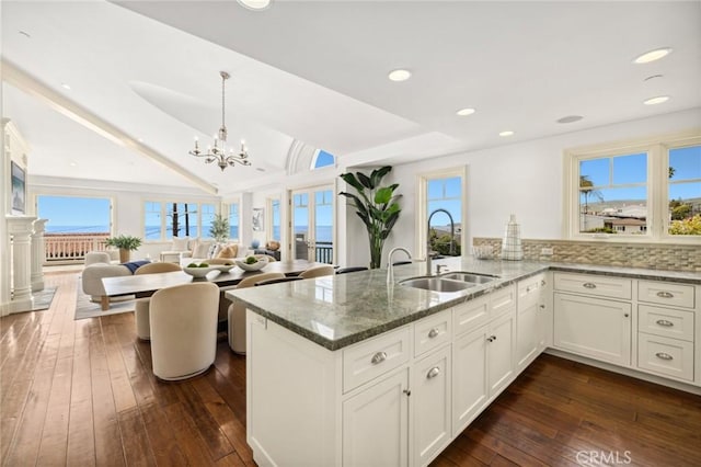 kitchen featuring white cabinets, dark wood-style flooring, a peninsula, stone counters, and a sink