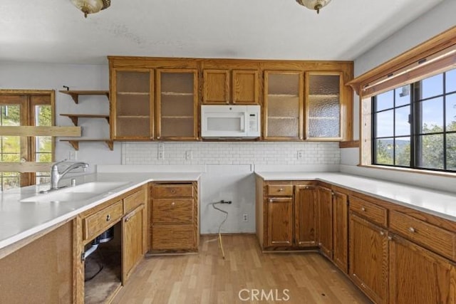 kitchen with light wood-type flooring, backsplash, a wealth of natural light, and sink