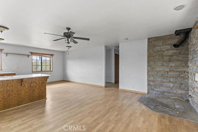 unfurnished living room featuring a wood stove, ceiling fan, and light wood-type flooring