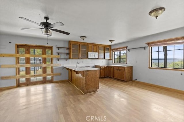 kitchen with ceiling fan, kitchen peninsula, light hardwood / wood-style floors, a kitchen bar, and decorative backsplash