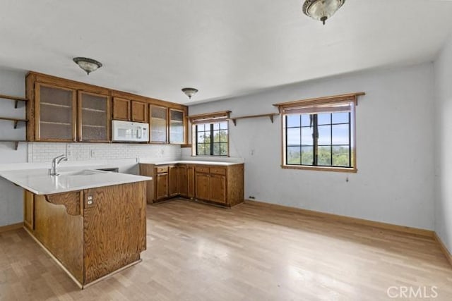 kitchen featuring backsplash, kitchen peninsula, sink, and light wood-type flooring