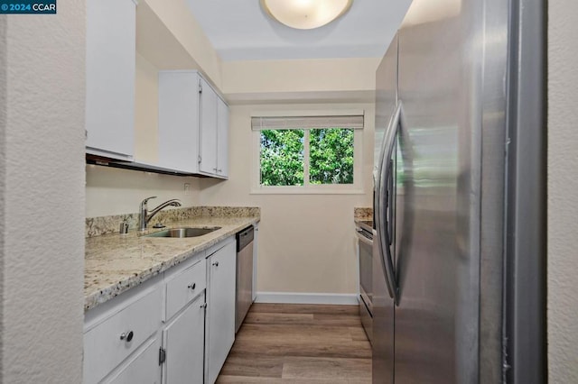 kitchen with wood-type flooring, white cabinets, sink, light stone counters, and appliances with stainless steel finishes