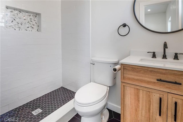 bathroom with toilet, tiled shower, and vanity