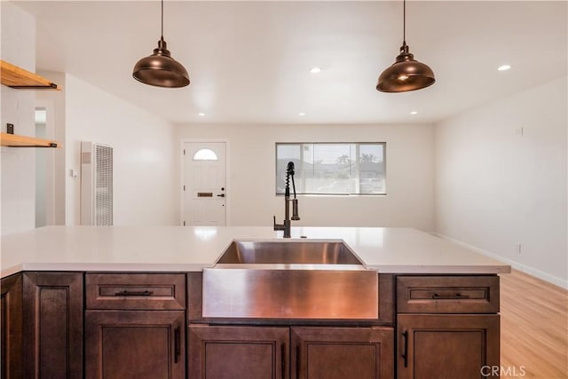 kitchen with open shelves, light countertops, dark brown cabinets, pendant lighting, and a sink