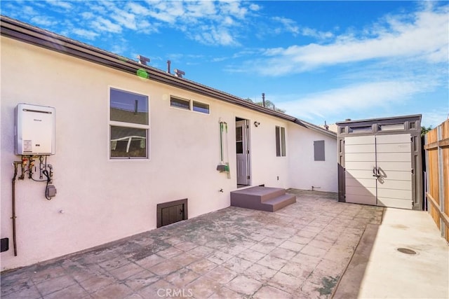 back of house featuring fence, tankless water heater, a patio, and stucco siding