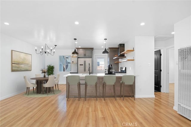 kitchen with light wood finished floors, open shelves, light countertops, appliances with stainless steel finishes, and wall chimney exhaust hood