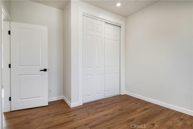 unfurnished bedroom featuring a closet, recessed lighting, wood finished floors, and baseboards