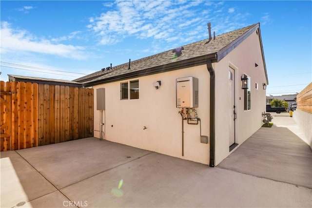 view of side of property featuring tankless water heater, a patio, fence, and stucco siding