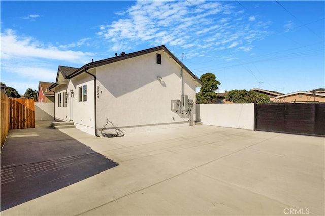 view of property exterior with a patio area, a gate, fence, and stucco siding