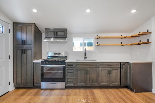 kitchen featuring under cabinet range hood, a sink, light countertops, open shelves, and stainless steel range with gas stovetop