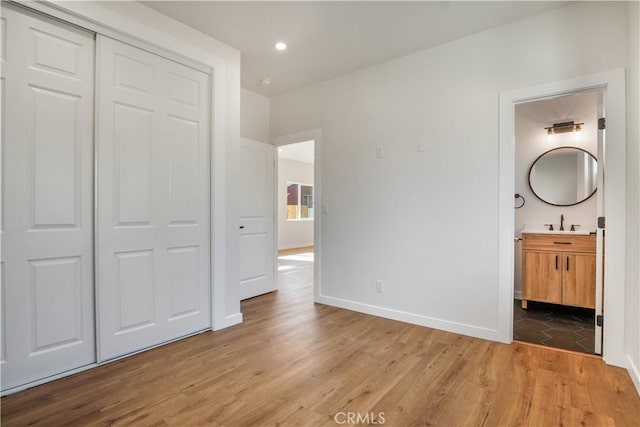 unfurnished bedroom with light wood finished floors, baseboards, ensuite bathroom, a sink, and a closet