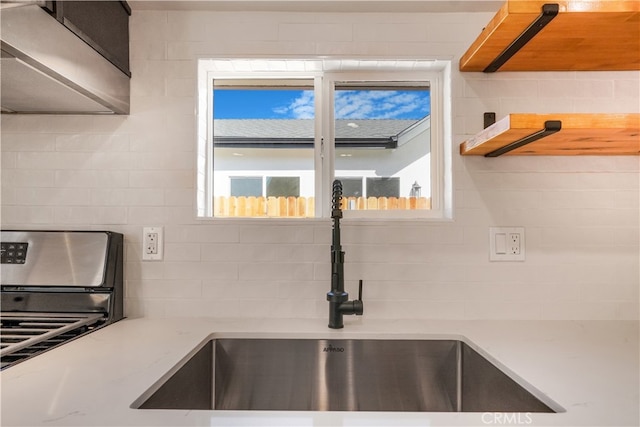 kitchen featuring exhaust hood, light stone counters, sink, and stainless steel stove