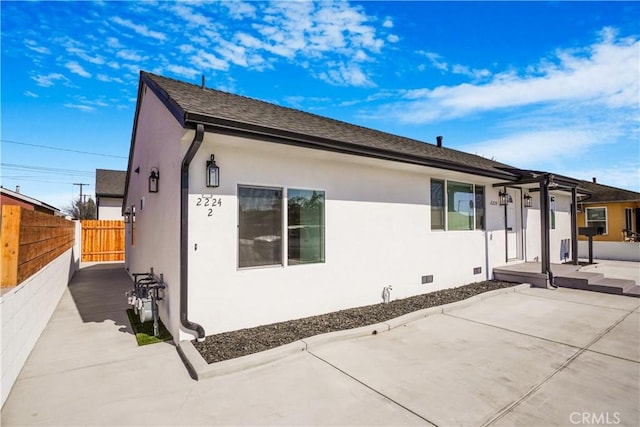 back of property featuring fence, roof with shingles, crawl space, stucco siding, and a patio area