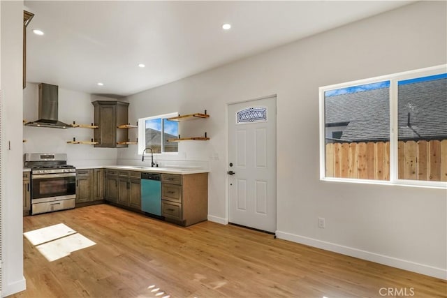 kitchen with light wood finished floors, wall chimney exhaust hood, open shelves, stainless steel gas range, and dishwashing machine