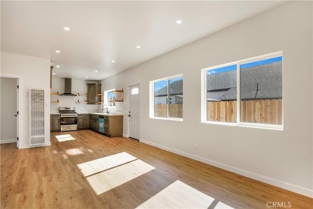 kitchen featuring light wood finished floors, open shelves, appliances with stainless steel finishes, a sink, and wall chimney range hood