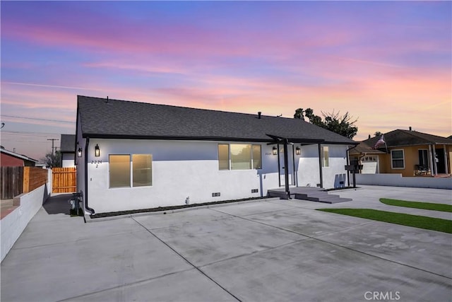 back of property at dusk featuring a shingled roof, fence, and stucco siding