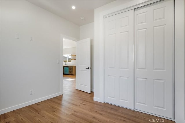 unfurnished bedroom with recessed lighting, a sink, baseboards, a closet, and light wood finished floors