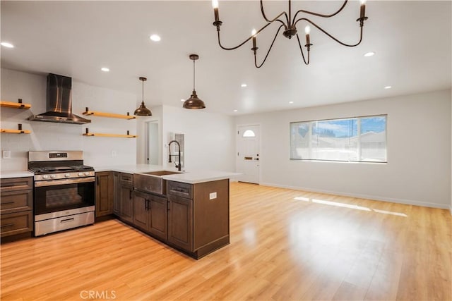 kitchen featuring gas range, light countertops, wall chimney range hood, open shelves, and a sink