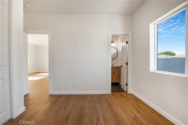 unfurnished bedroom featuring ensuite bath, baseboards, and wood finished floors