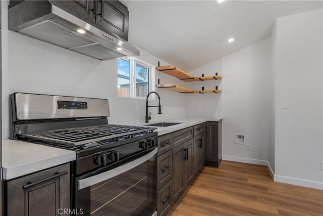 kitchen featuring baseboards, light wood-style flooring, stainless steel range with gas stovetop, extractor fan, and a sink