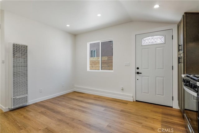 foyer featuring baseboards, a heating unit, vaulted ceiling, and light wood finished floors