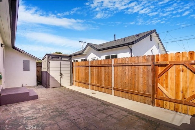 view of patio / terrace featuring an outbuilding, a storage unit, fence, and a gate