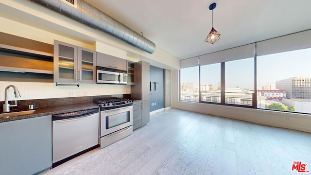 kitchen featuring appliances with stainless steel finishes, sink, dark stone countertops, light hardwood / wood-style floors, and hanging light fixtures