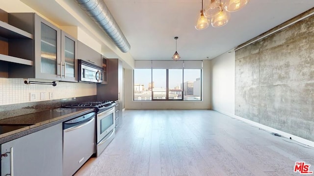 kitchen with hanging light fixtures, tasteful backsplash, dark stone counters, light hardwood / wood-style floors, and appliances with stainless steel finishes