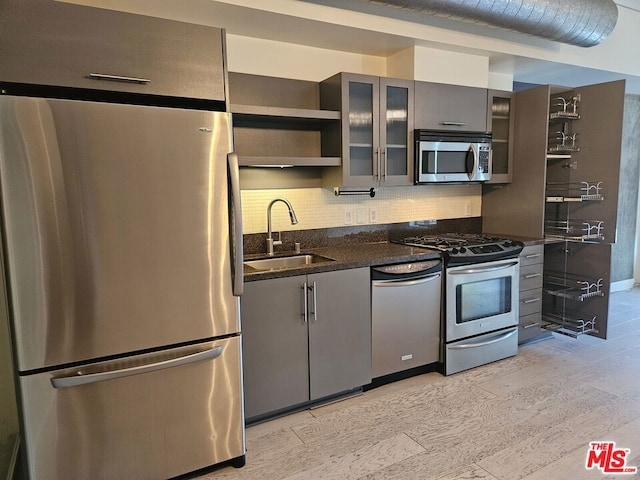 kitchen with sink, light hardwood / wood-style flooring, dark stone counters, decorative backsplash, and appliances with stainless steel finishes