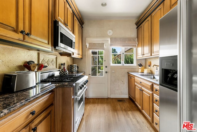 kitchen with sink, appliances with stainless steel finishes, light hardwood / wood-style flooring, and dark stone counters