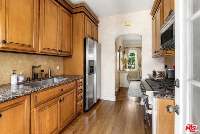 kitchen with stainless steel appliances, crown molding, dark stone counters, sink, and dark hardwood / wood-style flooring