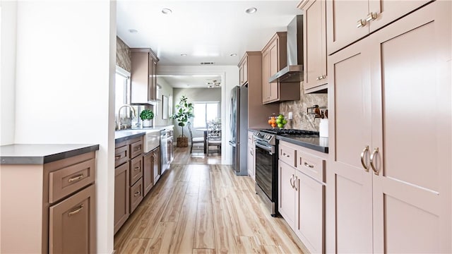 kitchen with sink, stainless steel appliances, wall chimney range hood, decorative backsplash, and light wood-type flooring