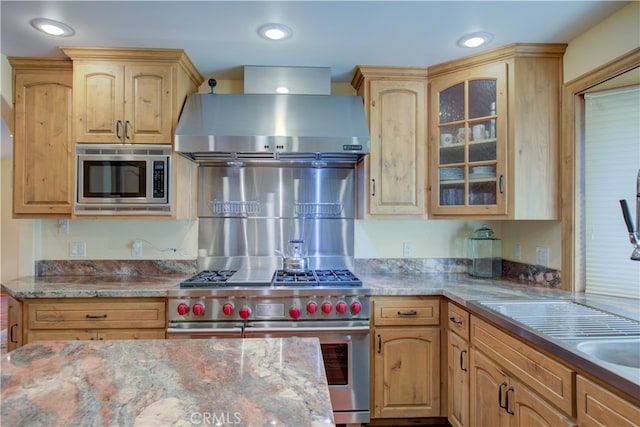 kitchen with appliances with stainless steel finishes, wall chimney exhaust hood, light stone countertops, and light brown cabinetry