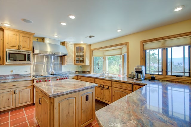 kitchen featuring appliances with stainless steel finishes, light brown cabinets, light stone countertops, and a center island