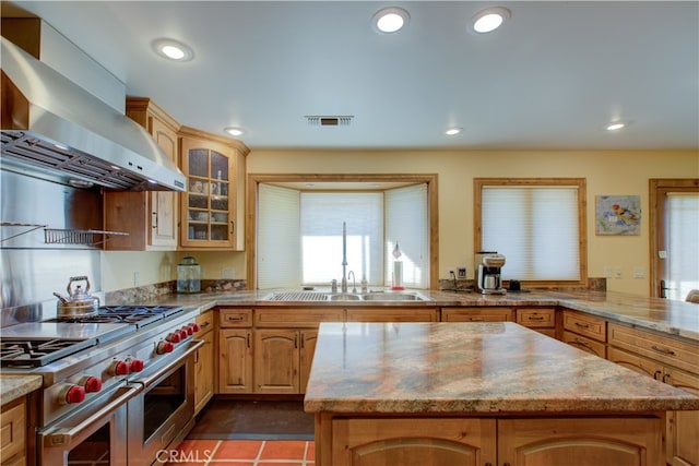 kitchen with wall chimney range hood, sink, kitchen peninsula, light stone counters, and double oven range