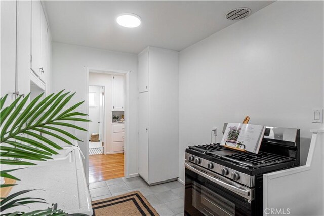 kitchen with white cabinets, light wood-type flooring, and stainless steel gas range oven