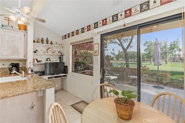 kitchen with light tile patterned flooring, sink, light stone counters, vaulted ceiling, and ceiling fan