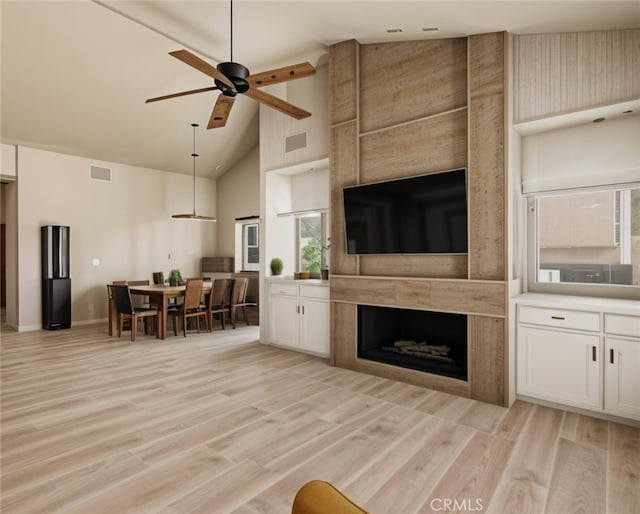 living room with ceiling fan, a large fireplace, high vaulted ceiling, and light hardwood / wood-style floors