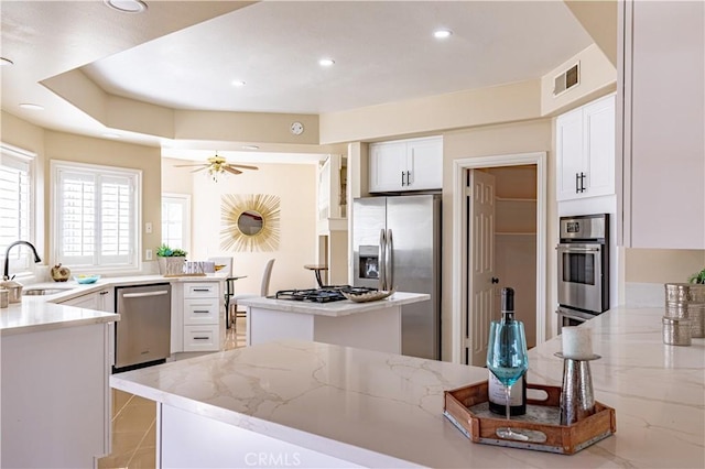 kitchen with light stone countertops, appliances with stainless steel finishes, ceiling fan, sink, and white cabinetry