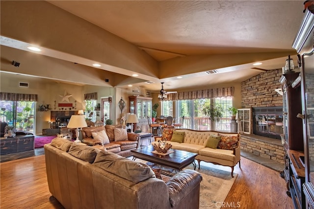 living room featuring vaulted ceiling, light hardwood / wood-style floors, a stone fireplace, and ceiling fan