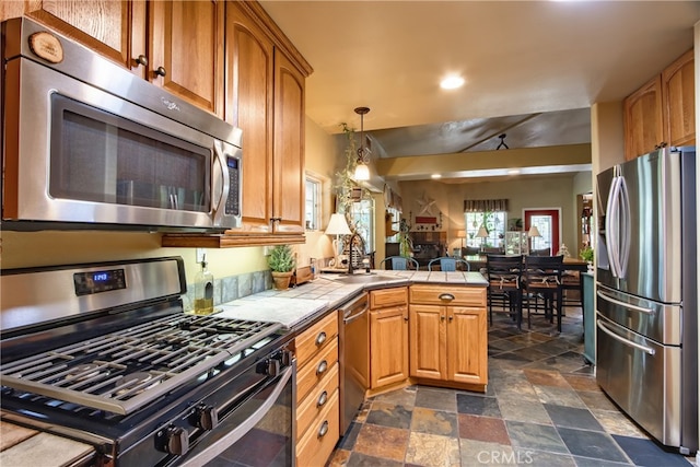 kitchen featuring kitchen peninsula, stainless steel appliances, sink, pendant lighting, and tile countertops