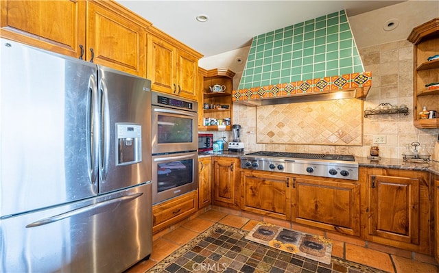 kitchen with tasteful backsplash, appliances with stainless steel finishes, dark stone countertops, and light tile flooring