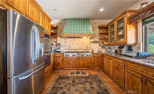 kitchen with appliances with stainless steel finishes, wall chimney range hood, backsplash, dark stone counters, and tile floors