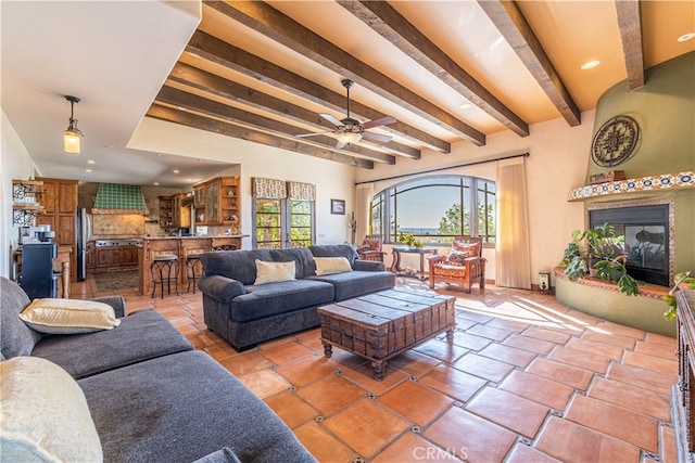 tiled living room featuring ceiling fan, beamed ceiling, and a large fireplace